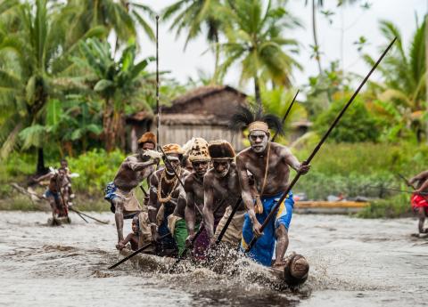 Asmat Tribe standing on wooden boat rowing